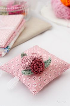 a pink pillow with a flower on it and some crochet work in the background