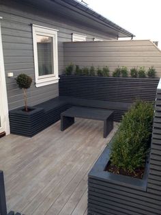 a wooden deck with benches and planters on the side of it in front of a house