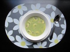 a white bowl filled with green soup on top of a floral table cloth next to a spoon