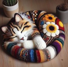 a cat laying on top of a multi colored knitted bed next to a potted plant