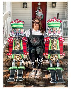 a woman sitting on the steps in front of a house with three large wooden figures