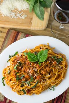 a plate of spaghetti with sauce and basil on top next to a glass of wine