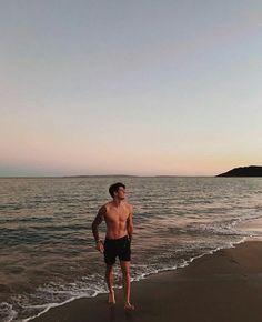 a man standing on top of a sandy beach next to the ocean at sunset or dawn