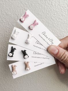 a person is holding four pairs of small animal studs in their hand, with the price tag below them