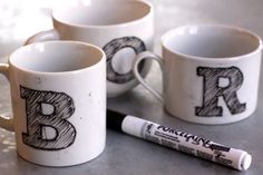 three coffee mugs with the letters b and person drawn on them next to a marker