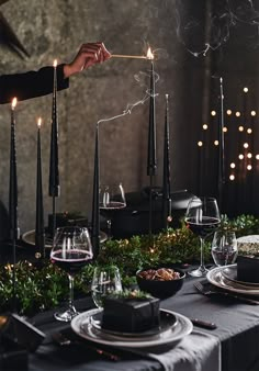 a person lighting candles on top of a table with plates and glasses in front of them