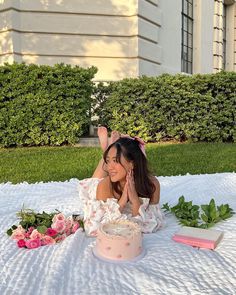 a woman laying on the ground next to a pink cake with white frosting and flowers