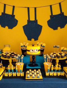 a yellow and blue dessert table with cupcakes, cake and decorations on it