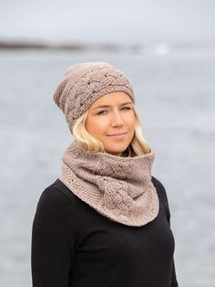 a woman standing by the water wearing a knitted hat and scarf with a cowl around her neck