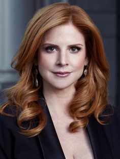 a woman with long red hair wearing a black jacket and posing in front of a building