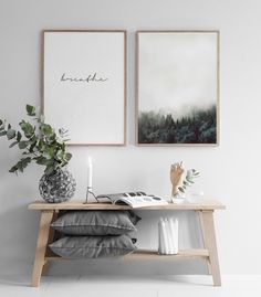 two pictures hanging on the wall above a wooden table with pillows and vases next to it