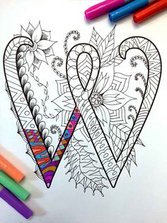 an adult coloring page with two hearts and flowers on it, surrounded by markers and crayons