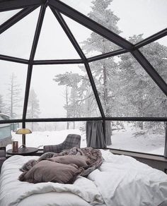 a bed sitting inside of a glass dome next to a window filled with snow covered trees