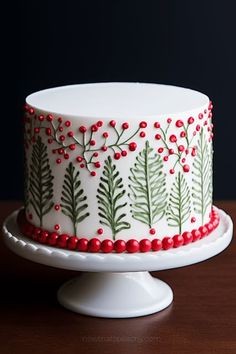 a white cake with red berries and green leaves on it, sitting on a wooden table