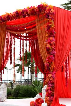 an orange and red wedding arch with flowers on the top, along with other decorations