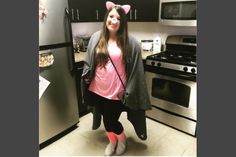 a woman standing in front of a refrigerator wearing a pink shirt and gray cardigan