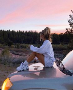 a woman sitting on top of a car in the middle of an open field at sunset