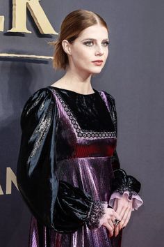 a woman in a black and purple dress standing on a red carpet with her hands in her pockets