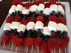 strawberries and blueberries are arranged on skewers with marshmallows