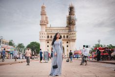 a woman standing in front of a large building with people walking around and onlookers