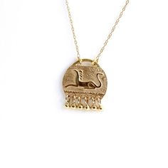 Gold hand engraved mythic animal pendant with necklace in solid gold with tiny gold dangles. A beautiful tribal necklace, fine hand work. The engrave mythic animal is a lion with bird's head. Pendant dimensions (without dangles): 10 x 12.5 mm | 0.38 x 0.49 inchMaterials: 14k solid gold (pendant & necklace).You can choose between two chain length options:1) Longer chain without clasp (to slip over your head, no fuss): 60 cm/23.622"2) Shorter chain with a gold clasp: 40 cm/15.748"Available in YELL Mythological Engraved Pendant Jewelry, Mythological Engraved Round Pendant Jewelry, Mythological Style Engraved Pendant Jewelry, Ancient Brass Pendant Jewelry, Ancient Style Brass Pendant Jewelry, Symbolic Carved Gold Jewelry, Ancient Style Ceremonial Pendant Necklaces, Ancient Yellow Gold Medallion Necklace, Gold Carved Round Pendant Necklace