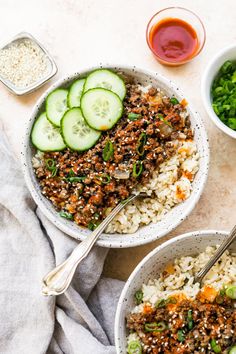 two bowls filled with rice, cucumbers and sauces on top of a table