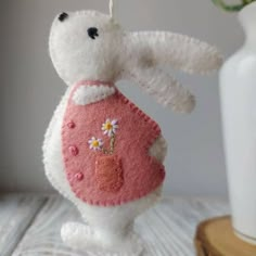 a white stuffed animal wearing a pink sweater with daisies on it's chest