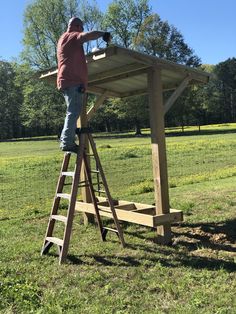 a man standing on top of a ladder next to a wooden table in the grass