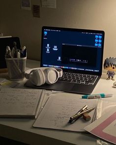 an open laptop computer sitting on top of a desk next to headphones and pens