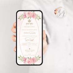 a person holding up a phone with a wedding card on the screen and flowers around it