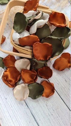 several pieces of cloth flowers in a basket on a white wooden table with green leaves