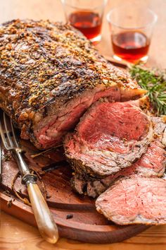 a large piece of meat sitting on top of a wooden cutting board next to some wine glasses