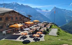 tables and umbrellas on the side of a mountain with mountains in the background,