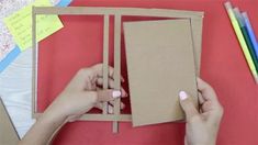 two hands are holding a piece of cardboard and some colored pencils on a table