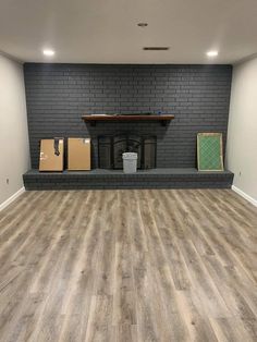 an empty room with hard wood flooring and grey brick wall behind the fireplace area