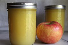 two jars with yellow liquid and an apple