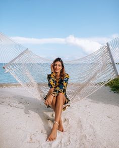 a woman sitting in a hammock on the beach with her feet propped up