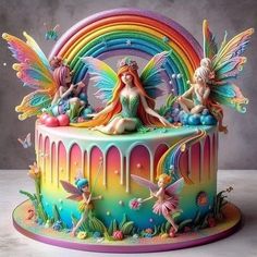 a cake decorated with fairy figurines sitting on top of rainbow colored icing