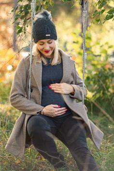 a pregnant woman sitting on a swing with her belly in the air and wearing a hat