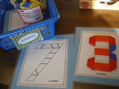 the number 3 is made out of construction paper and plastic blocks, next to a shopping basket