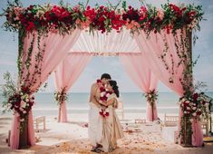 two people standing in front of a pink and white wedding arch with flowers on it