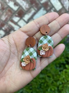 a hand holding two small wooden earrings with flowers on them in front of a brick wall