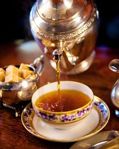 tea being poured into a cup with sugar cubes in the foreground and a silver tea pot behind it on a wooden table