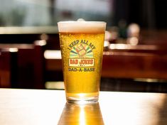 a beer glass sitting on top of a wooden table in a restaurant or bar with the words dad - a - base printed on it