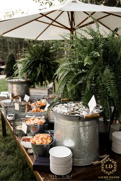 an outdoor buffet is set up with silver buckets and plates