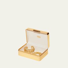 an open box with two gold bracelets in it on a white surface and the lid opened