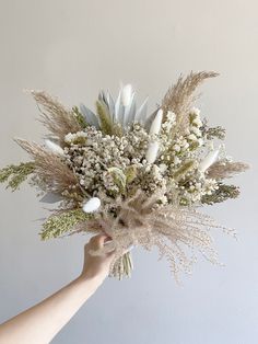 a hand holding a bouquet of flowers in front of a white wall with no one around it