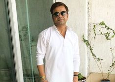 a man in white shirt and sunglasses standing next to a wall with ivy growing on it