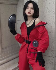 a woman in a red jumpsuit is holding a black helmet and looking at the camera