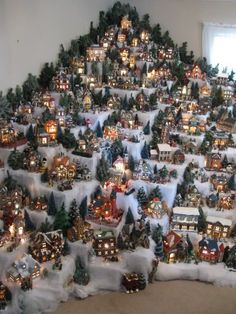 a christmas tree made out of fake snow with lights and houses on it in front of a window